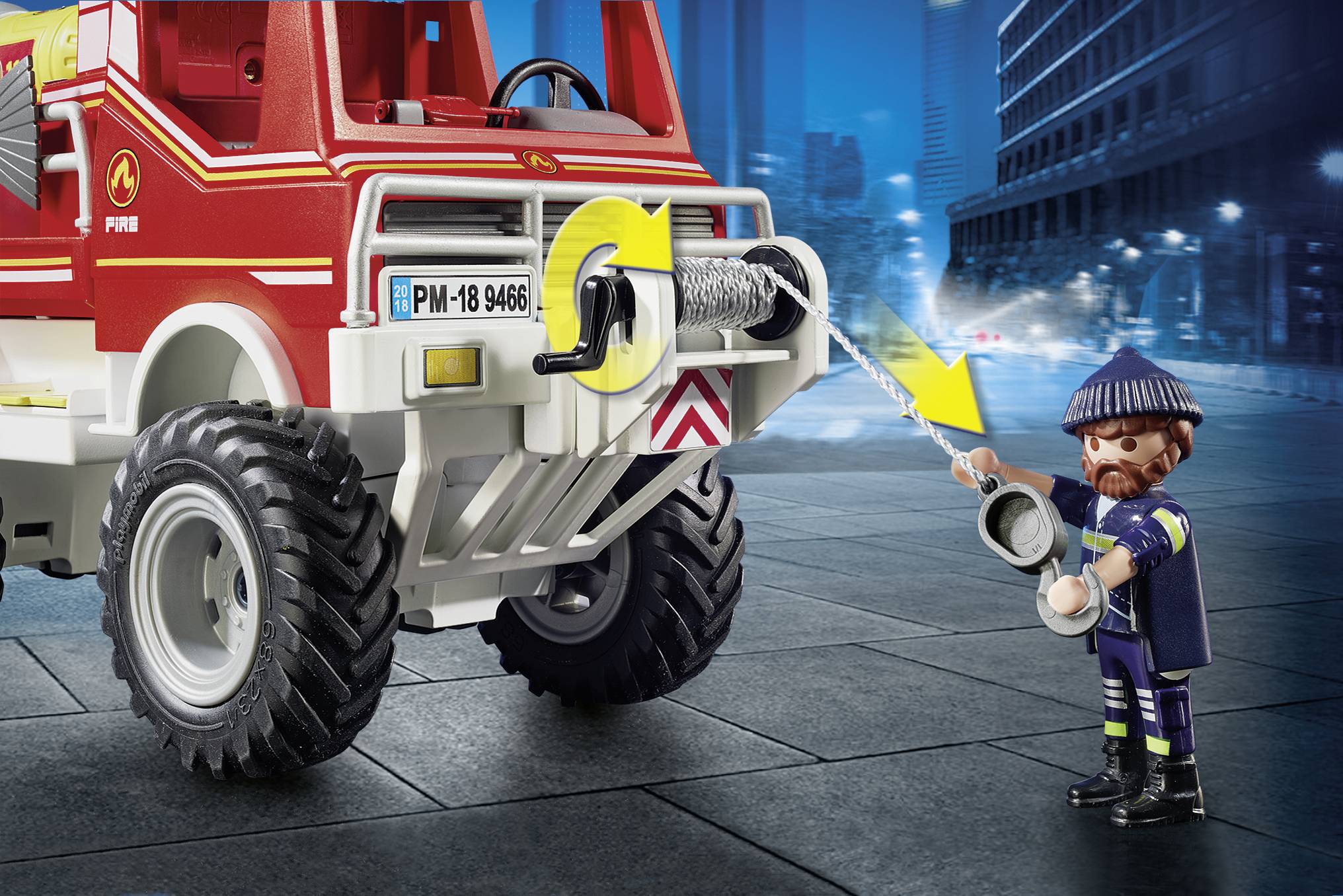 Ein Feuerwehrmann-Spielzeug zieht ein Kabel aus einem roten Feuerwehrfahrzeug. Das Fahrzeug steht auf einer dunklen Straße in der Stadt.