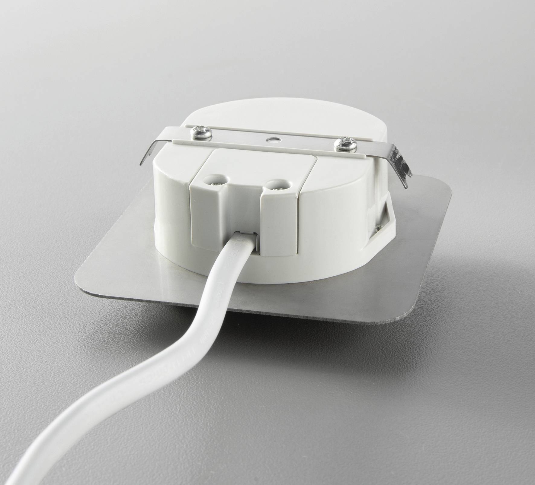 Ein weißer runder Sensor mit Kabelanschluss auf einer grauen Oberfläche. Der Sensor hat eine Metallklammer zur Befestigung.