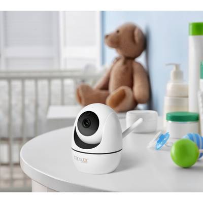 Eine Baby-Kamera steht auf einem Tisch im Kinderzimmer, daneben Spielzeug und Pflegeprodukte. Im Hintergrund ein Teddybär und ein Kinderbett.