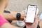 Person überprüft Fitnessdaten auf Smartwatch und Smartphone. Die Smartwatch zeigt Schrittanzahl, das Smartphone weitere Aktivitätsdaten.