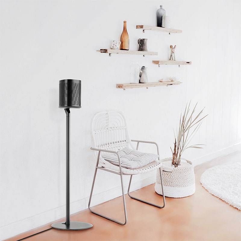 Helles Wohnzimmer mit weißem Stuhl, schwarzer Stehlampe und Regalen an der Wand. Pflanzen tragen zur Dekoration bei.