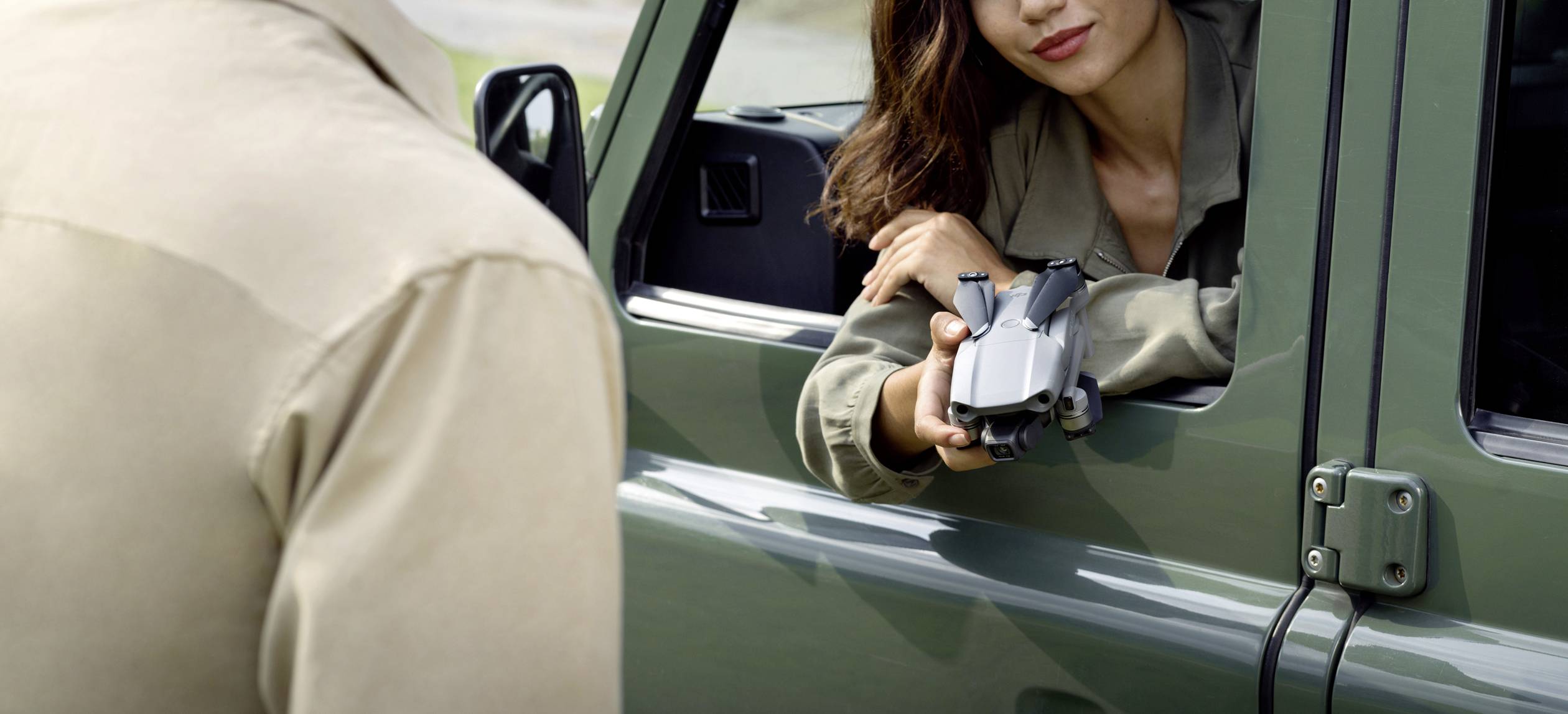 Eine Person in einem Auto reicht einer anderen Person eine Kamera durch das Fenster.