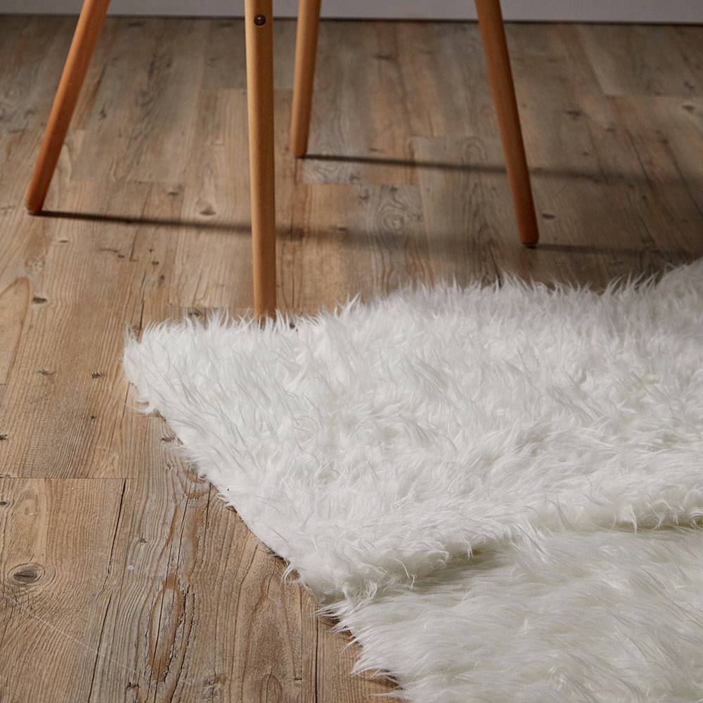 Ein Stuhl mit Holzbeinen steht auf einem Holzboden, neben einem weißen, flauschigen Teppich.