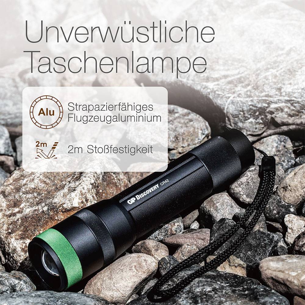 Eine schwarze Taschenlampe mit grünem Ring liegt auf Steinen. Text: 'Unverwüstliche Taschenlampe', 'Strapazierfähiges Flugzeugaluminium', '2m Stoßfestigkeit'.