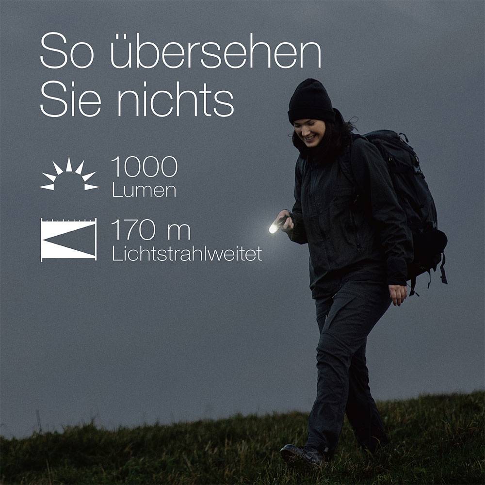 'Person mit Taschenlampe unterwegs. Text beschreibt Lichtleistung: 1000 Lumen und Reichweite: 170 m. Überschrift: So übersehen Sie nichts.'