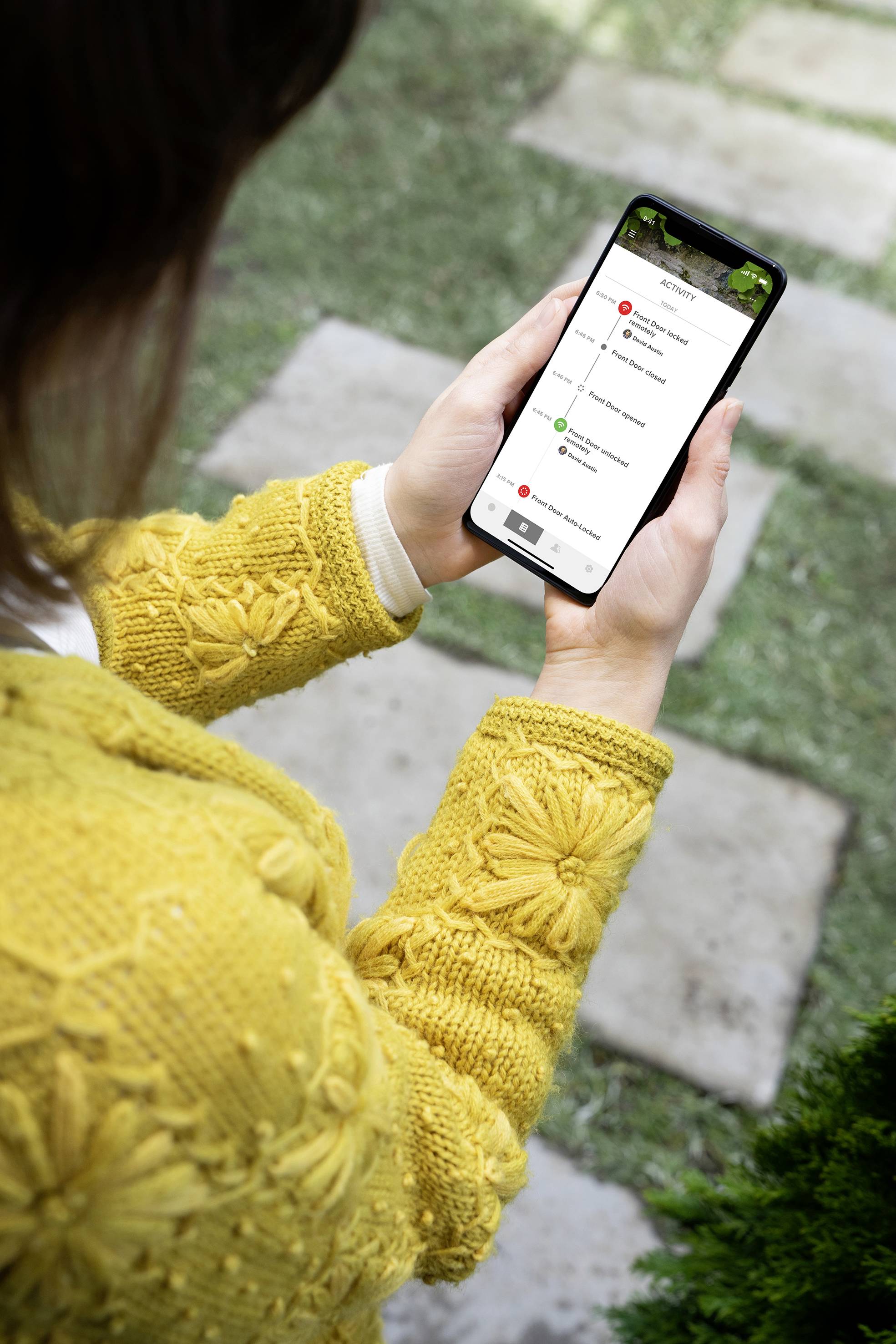 Eine Person in einem gelben Pullover hält ein Smartphone, auf dem eine Navigations-App mit einem hervorgehobenen Reiseziel angezeigt wird.