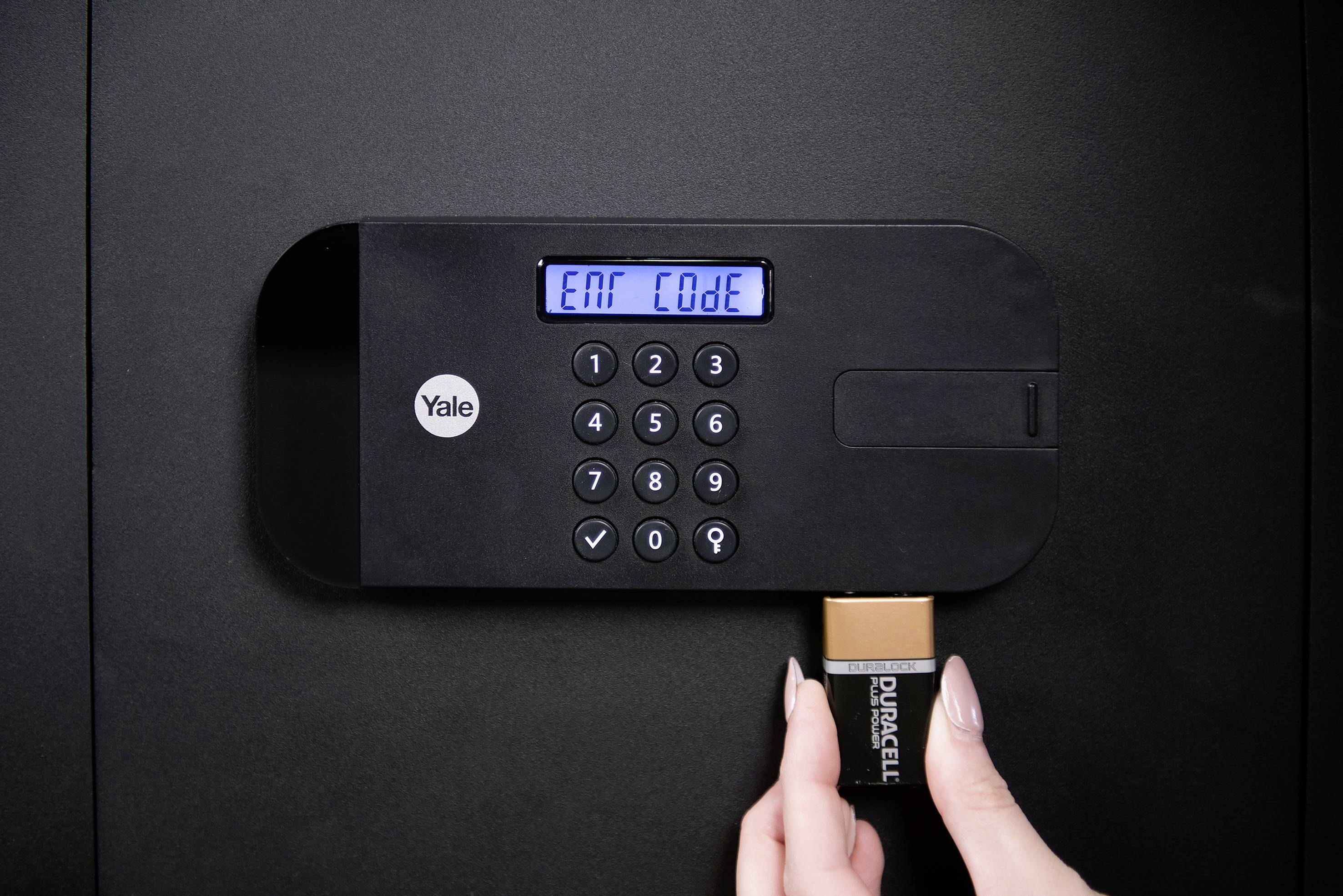 Hand wechselt Batterie in elektronischem Safe mit Display 'Ent Code'. Sicherheitsgefühl und Wartung im Fokus.