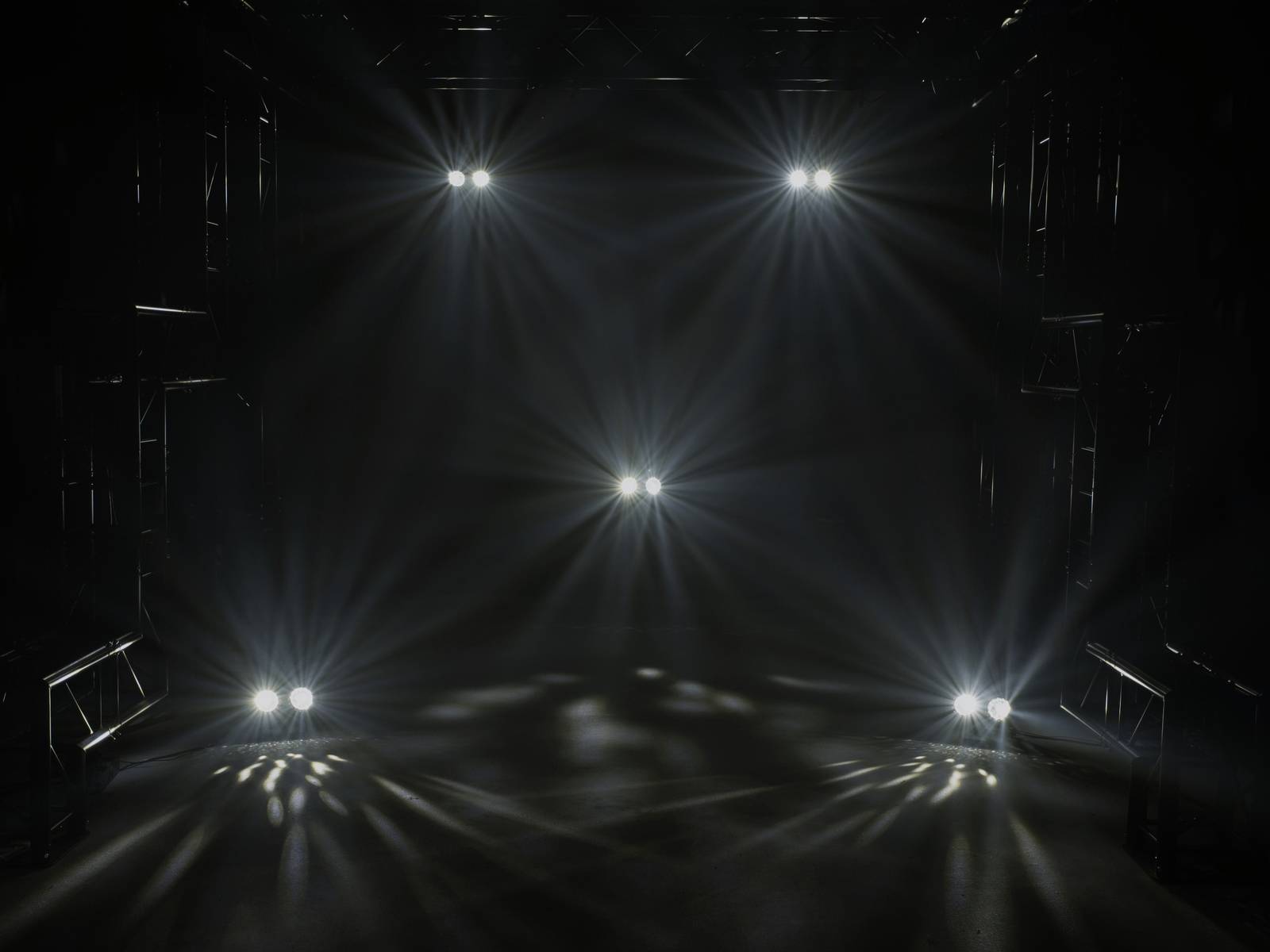 'Dunkle Bühne mit hellen Scheinwerfern, die in verschiedene Richtungen leuchten, und dunklem Hintergrund.'