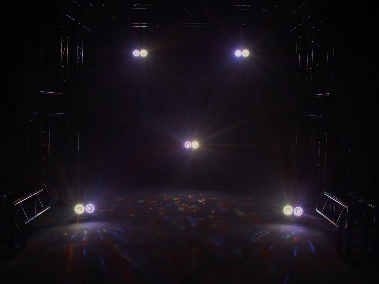 Im Bild sind sechs helle Lichtstrahler in einem dunklen Raum zu sehen, die den Boden beleuchten und ein Bühnenset andeuten.