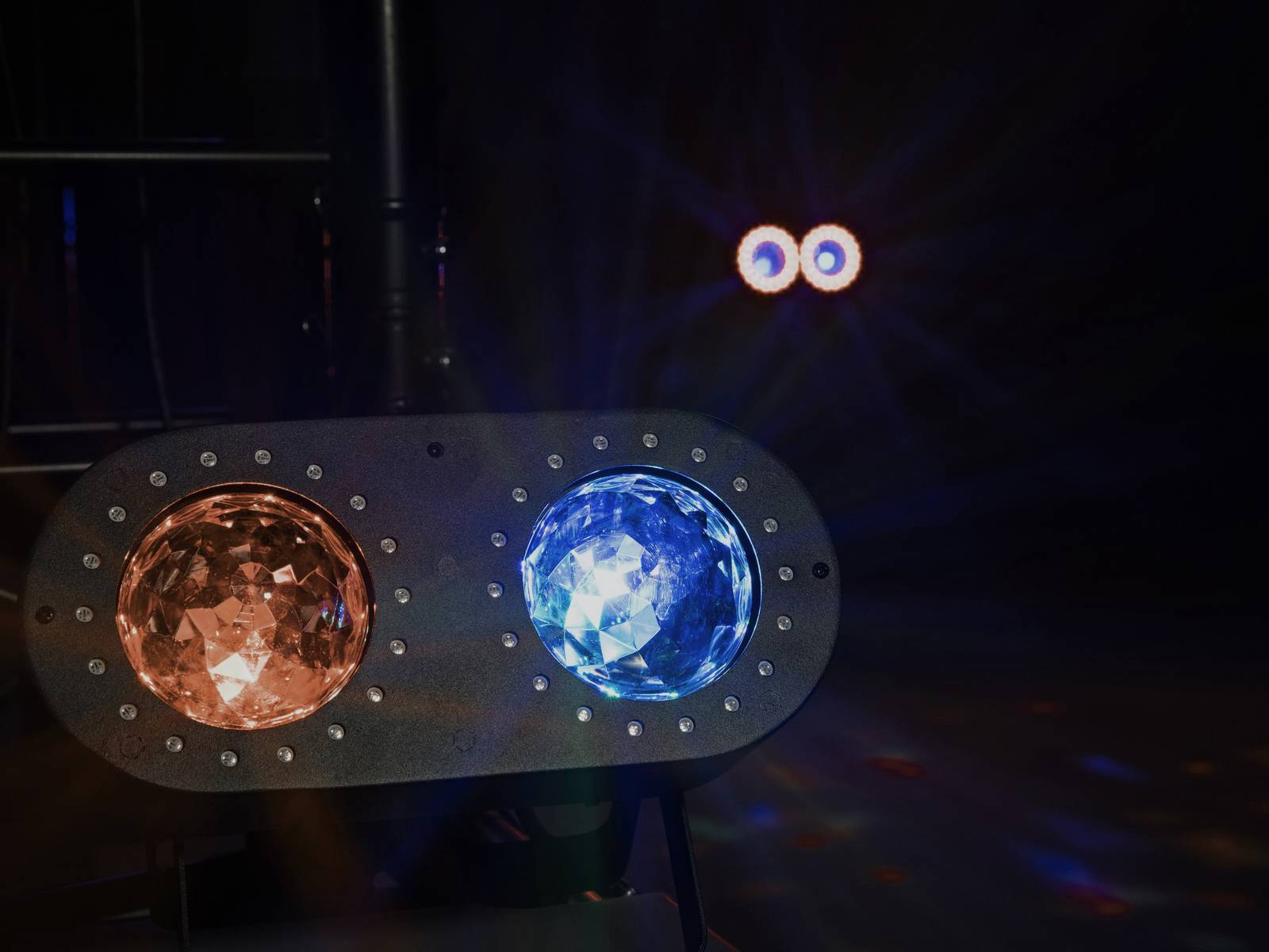 Lichtmaschine mit zwei bunten Lichtern: links orange, rechts blau. Dunkler Hintergrund, einige diffuse Lichtreflexionen sichtbar.