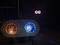 Lichtmaschine mit zwei bunten Lichtern: links orange, rechts blau. Dunkler Hintergrund, einige diffuse Lichtreflexionen sichtbar.