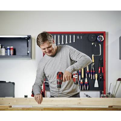 Ein Mann bohrt mit einem Akkubohrer in ein Holzbrett. Im Hintergrund hängt Werkzeug an einer Wand.