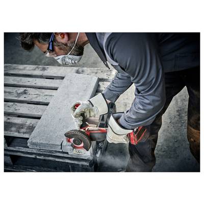 Arbeiter, der Schutzbrille und Handschuhe trägt, schneidet eine Betonplatte mit einem tragbaren Winkelschleifers, wobei Staub entsteht.