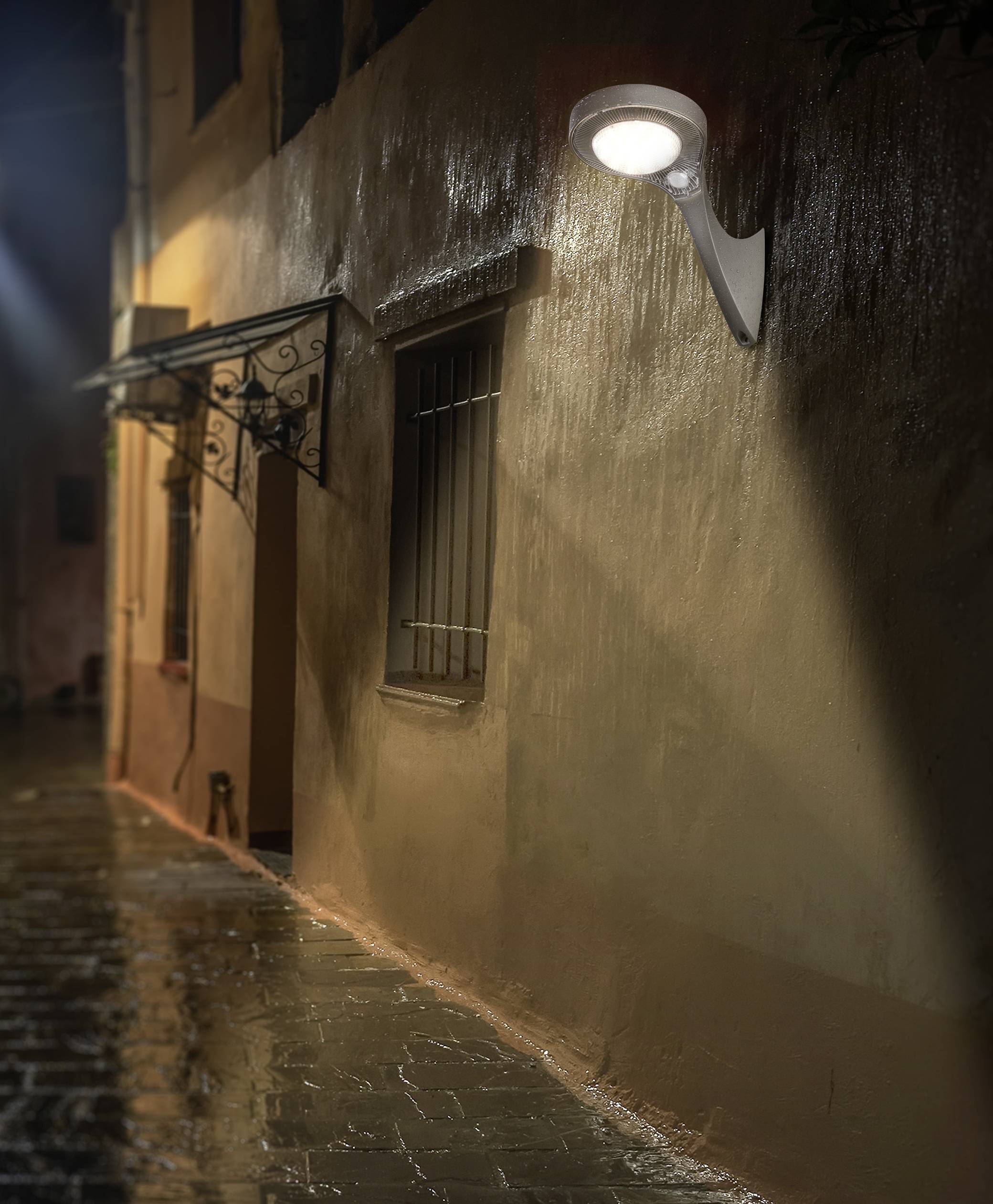 Eine beleuchtete Gasse bei Nacht. Eine Straßenlaterne wirft warmes Licht auf eine nasse, menschenleere Straße neben einem Gebäude.