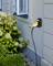 'Außensteckdose an einer Hauswand mit einem eingesteckten Kabel im Garten, umgeben von Hortensien und Kieselsteinen.'
