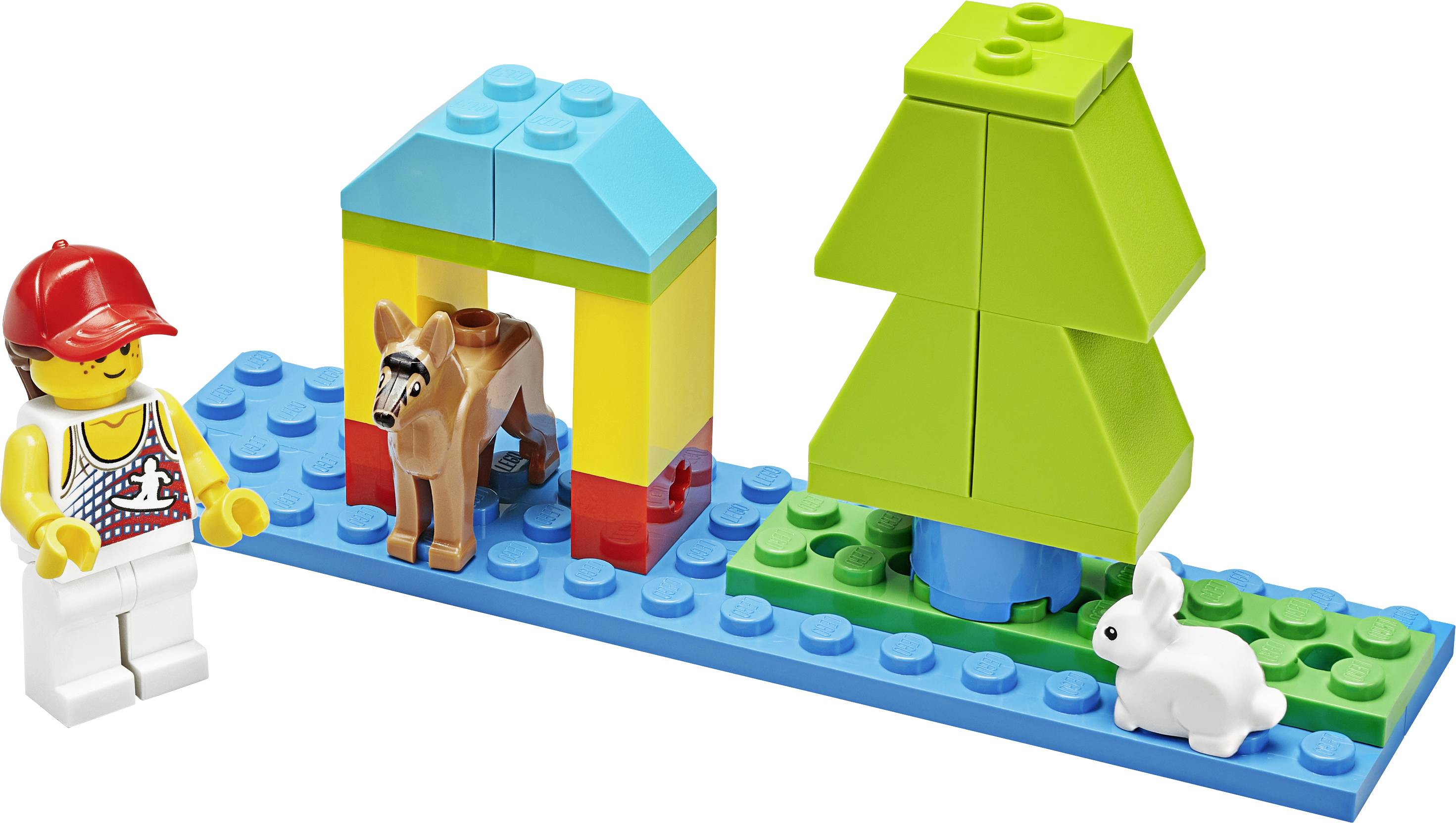 Spielzeug-Lego-Szene mit Figur, kleinem Stall mit Esel und Baum auf blauer Plattform. Ein weißes Kaninchen sitzt daneben.