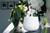Ein weißer Luftbefeuchter verbreitet Dampf neben einer Vase mit Orchideen auf einem Tisch mit weicher Beleuchtung im Hintergrund.