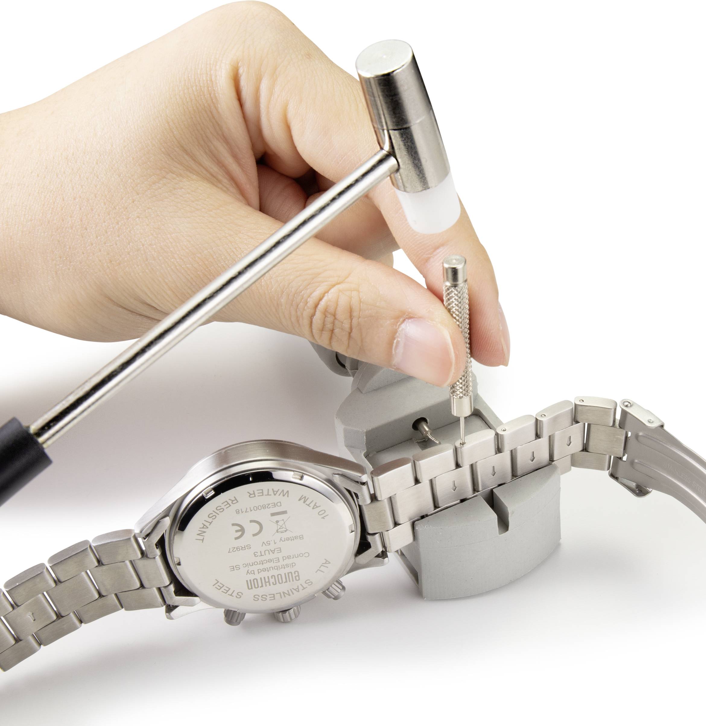 Eine Hand hält ein Uhrenarmband-Werkzeug und entfernt einen Stift aus dem Metallarmband einer Uhr, die in einem Halter fixiert ist.