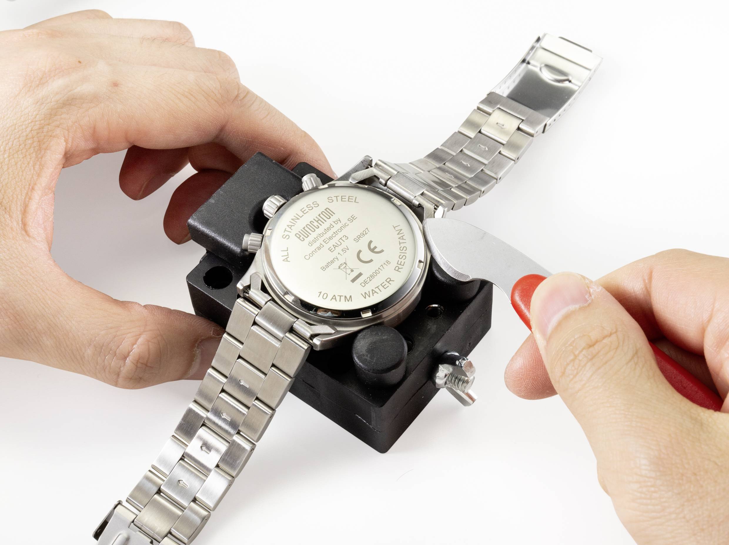 'Eine Person öffnet die Rückseite einer Armbanduhr mit einem Werkzeug, um sie zu reparieren oder die Batterie zu wechseln.'