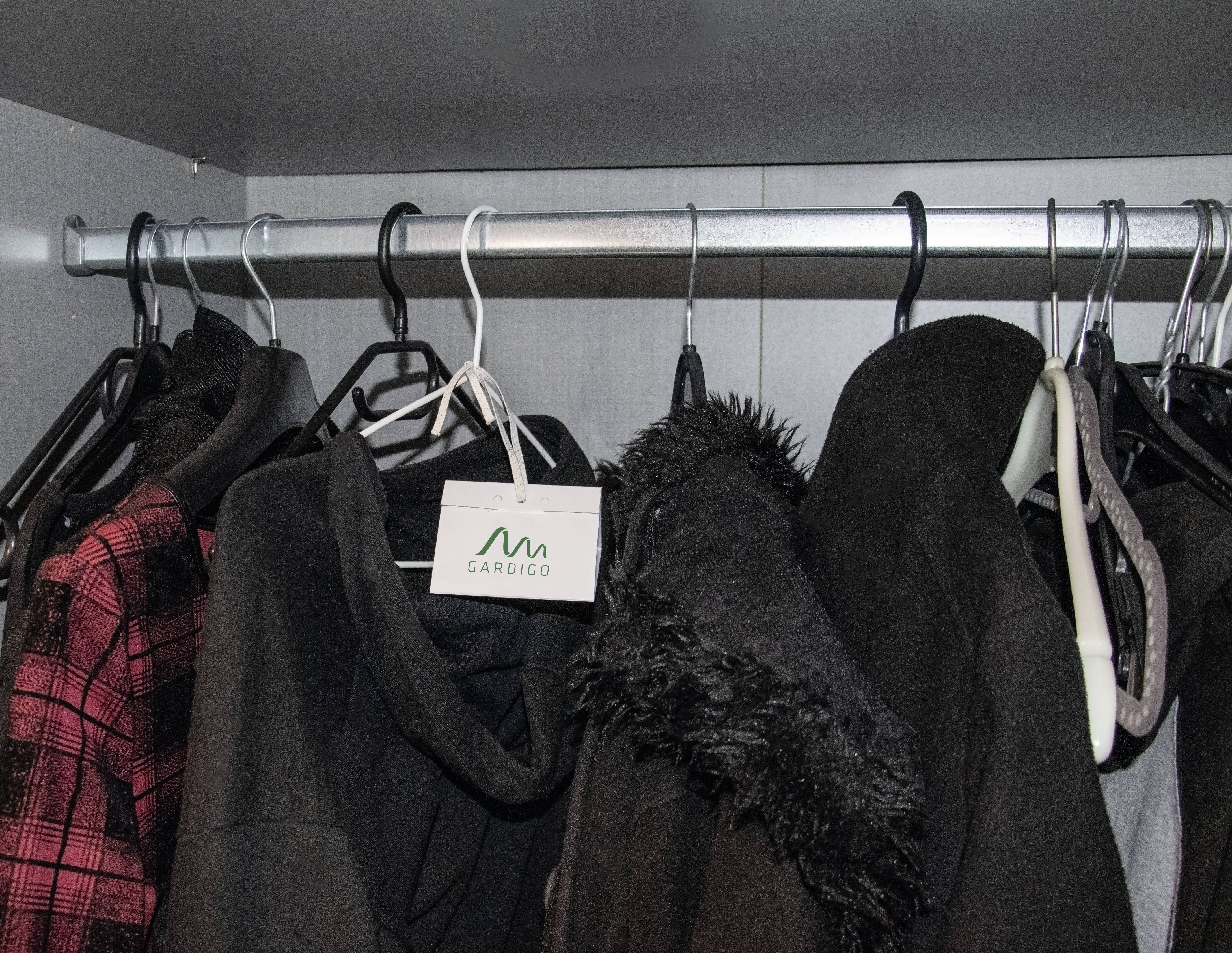 Verschiedene Jacken hängen an Kleiderbügeln in einem Schrank. Ein weißes Etikett mit der Aufschrift 'CARDIGO' ist sichtbar.