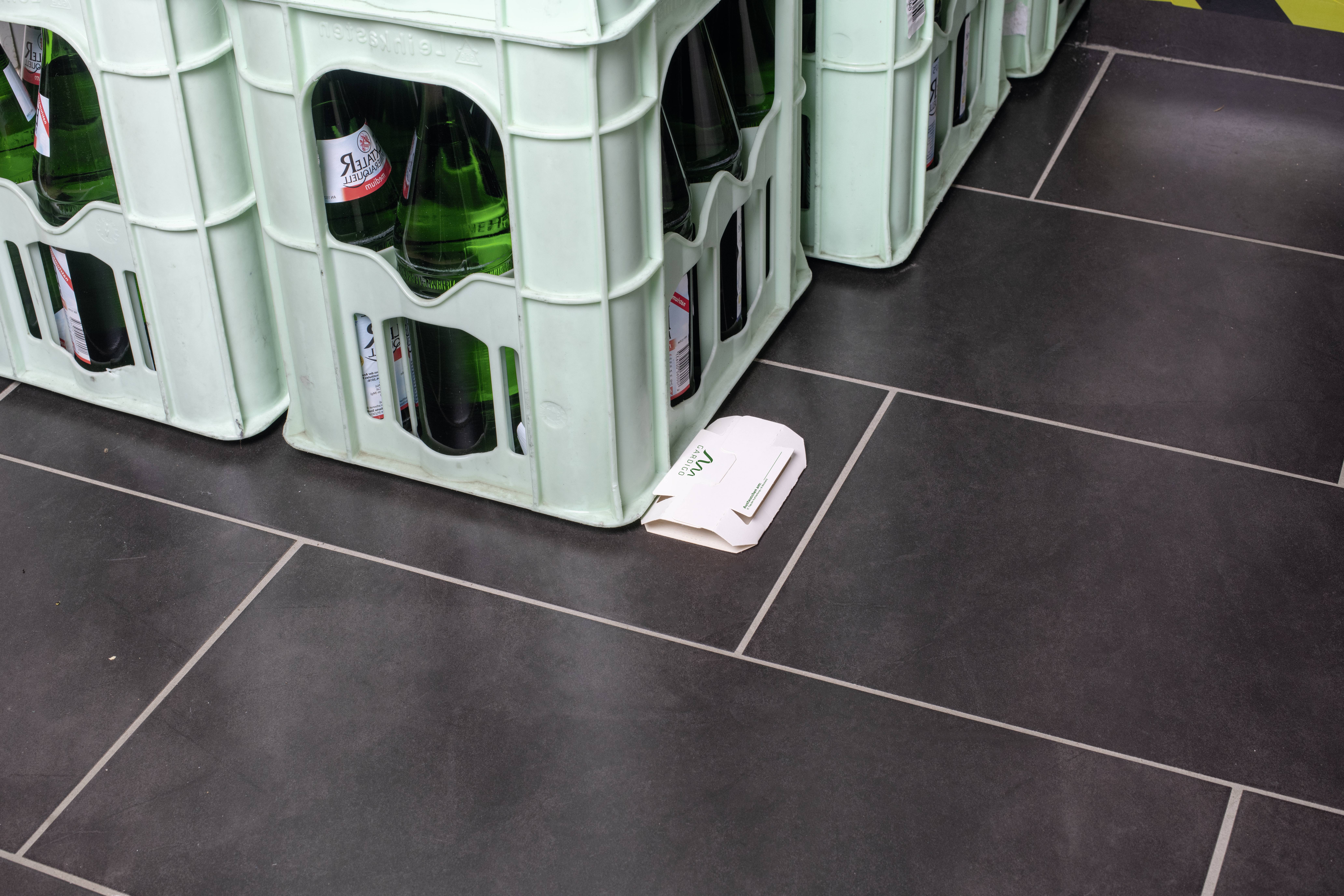 Leere Getränkekisten aus Plastik stehen auf einem dunklen Fliesenboden. Daneben liegt ein weißes Tuch.