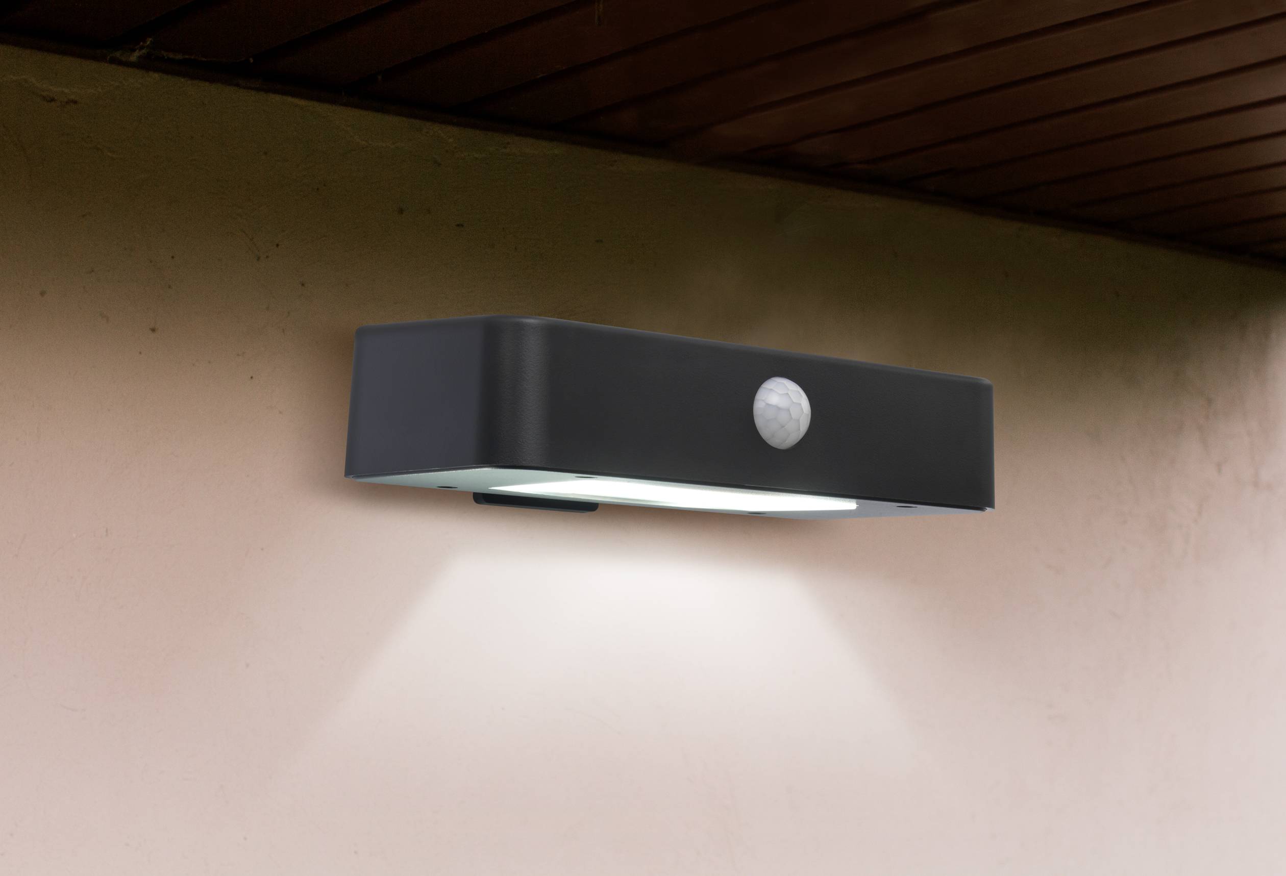 Eine moderne Außenleuchte mit Bewegungssensor leuchtet an einer Hauswand. Sie strahlt Licht nach unten und sorgt für Beleuchtung im Dunkeln.