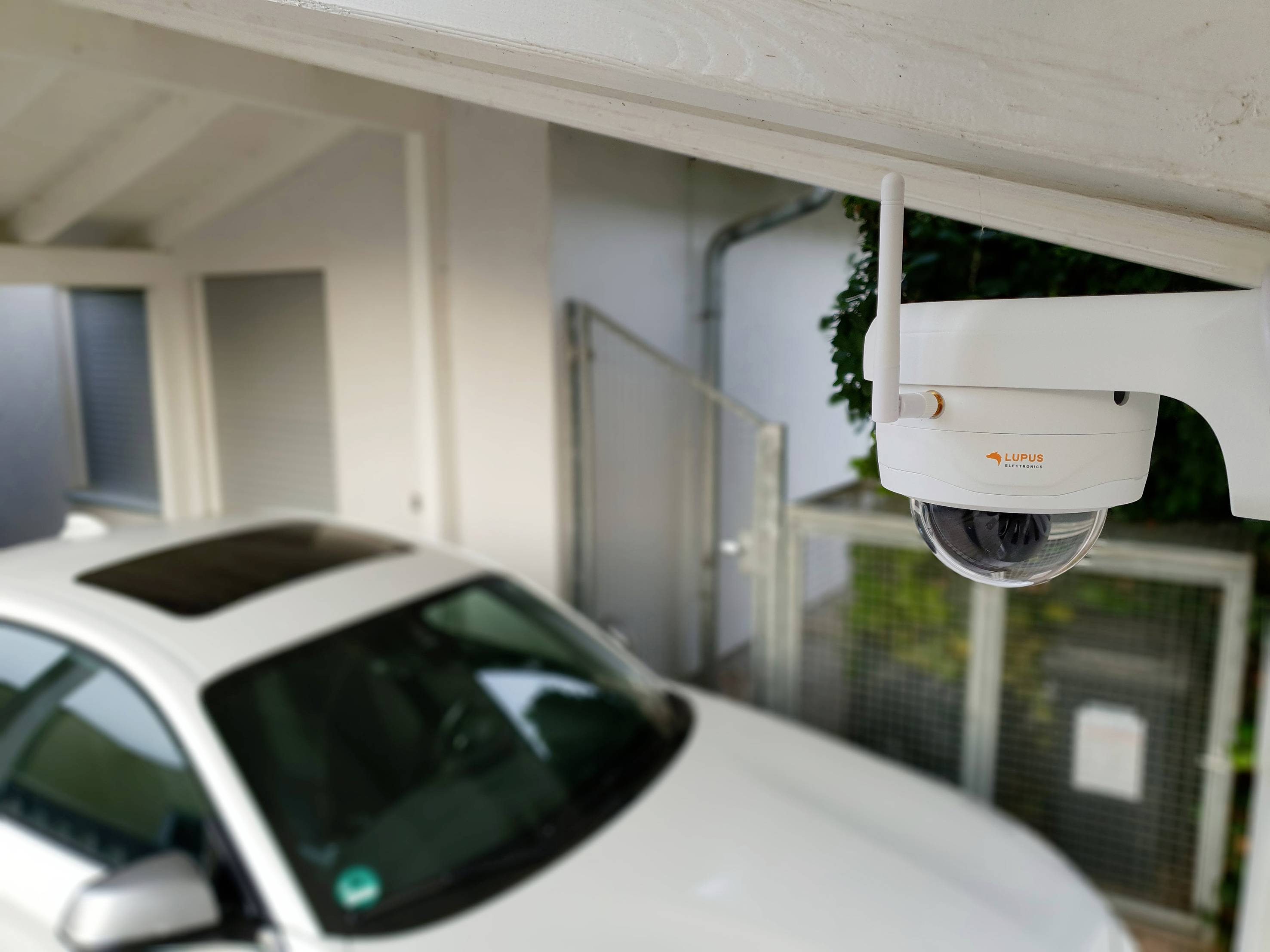 Überwachungskamera in einer Garage mit Blick auf ein geparktes weißes Auto. Kamera fokussiert auf Sicherheitsüberwachung.