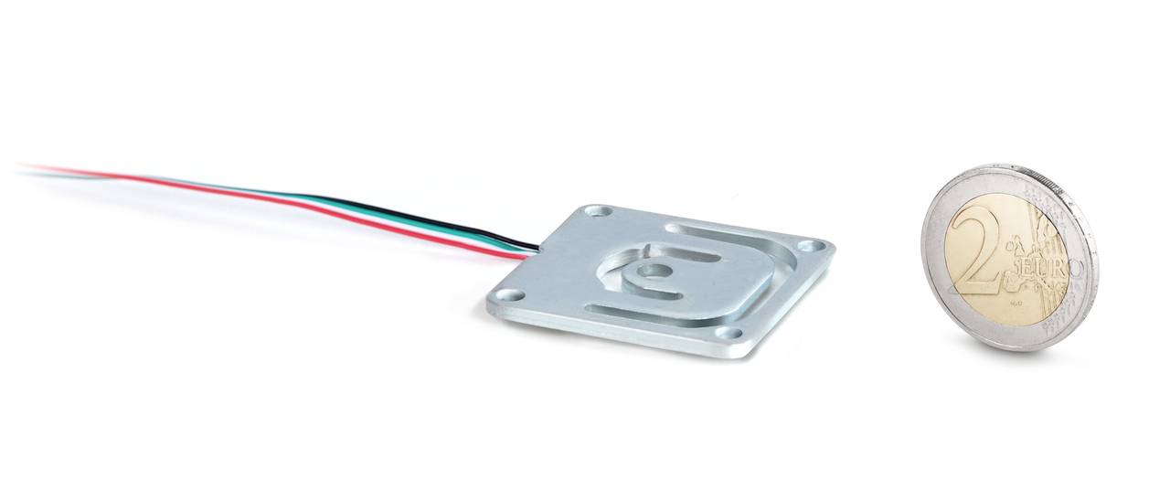'Flacher quadratischer Drucksensor mit bunten Kabeln links neben einer 2-Euro-Münze zum Größenvergleich auf weißem Hintergrund.'