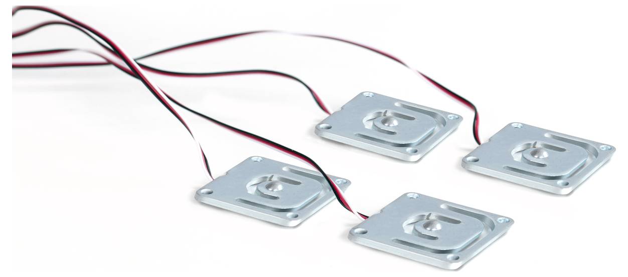 Vier quadratische Metallplatten mit roten und schwarzen Kabeln, wahrscheinlich elektronische Sensoren oder Gerätekomponenten, auf weißem Hintergrund.