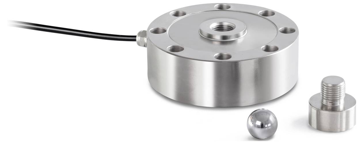 Ein runder Kraftsensor aus Metall mit Kabelanschluss zeigt die Funktion mechanischer Messungen. Daneben liegen eine Metallkugel und ein Bolzen.