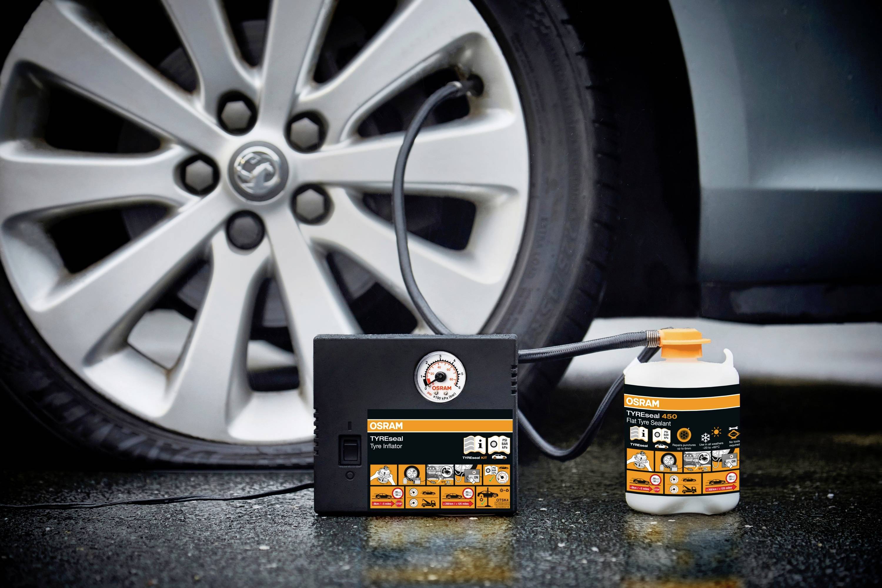 Ein Reifenpannenset mit Kompressor und Dichtmittel steht vor einem Autoreifen. Das Set ist bereit zur Reifenreparatur.