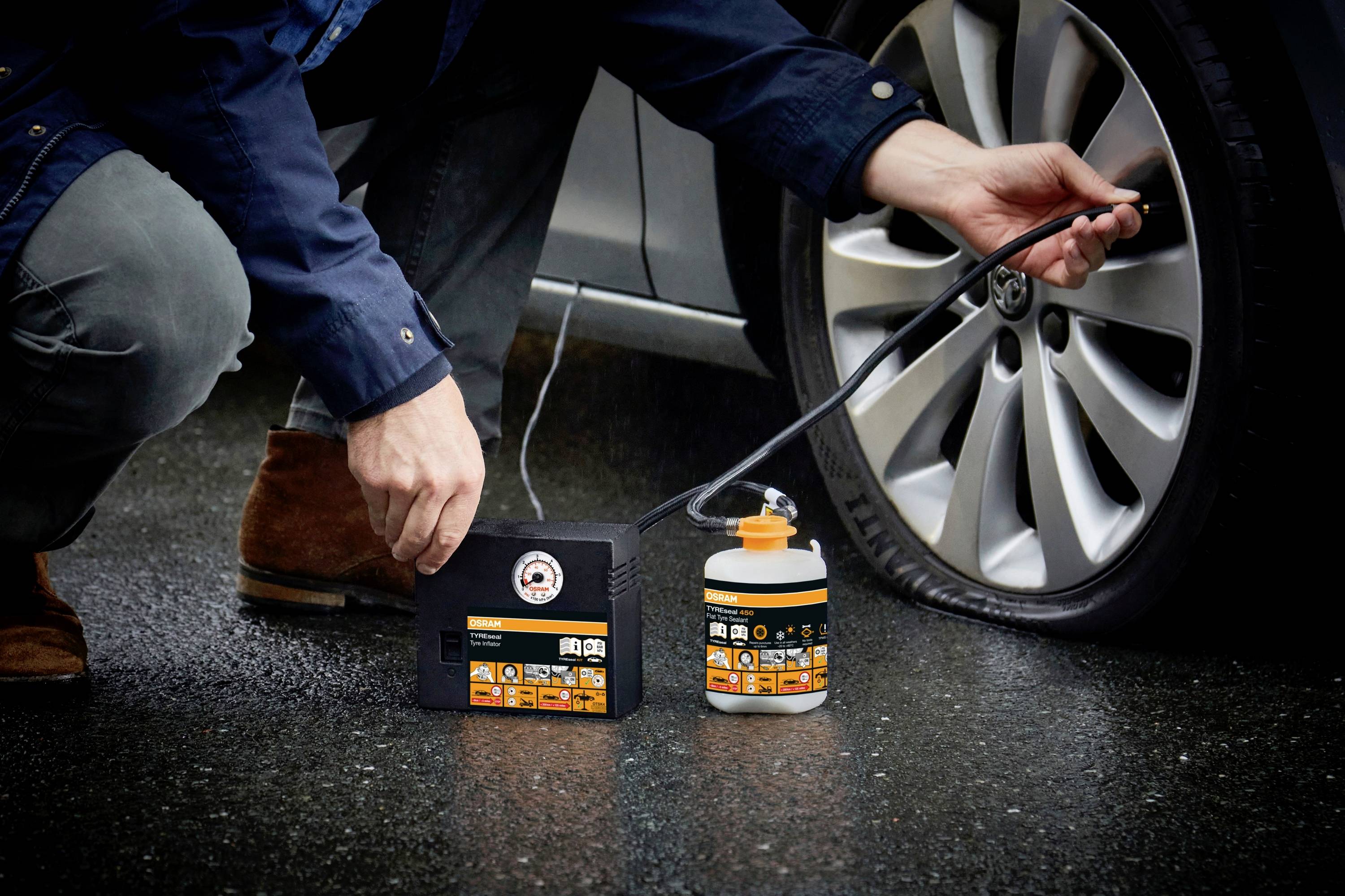 Person pumpt Reifen eines Autos am Straßenrand auf, verwendet tragbaren Kompressor und Dichtmittel. Reifen wird repariert.