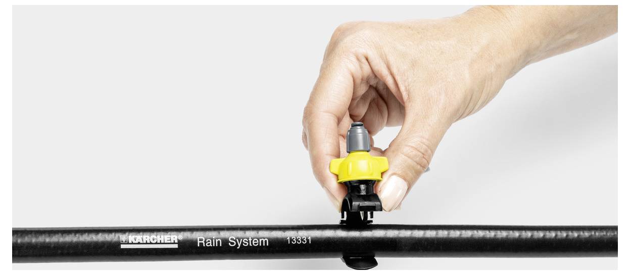 Eine Hand, die ein gelbes Ventil an einem Kärcher-Regensystem-Schlauch einstellt, was den Aufbau des Bewässerungssystems anzeigt.
