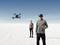 Ein Mann mit VR-Brille fliegt eine Drohne in einer weiten weißen Landschaft, daneben steht eine Frau. Der Himmel ist klar und blau.