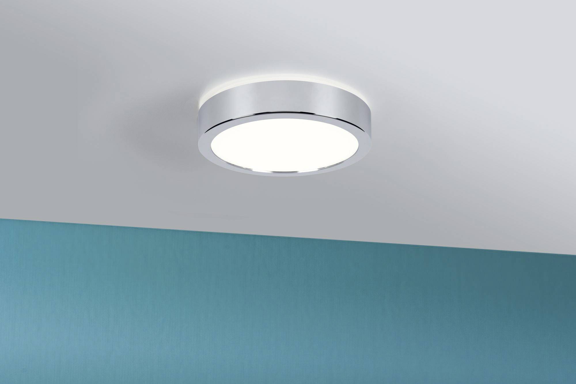 Runde Deckenleuchte mit Metallrahmen, die ein gleichmäßiges, weiches Licht auf eine türkisfarbene Wand und Decke strahlt.