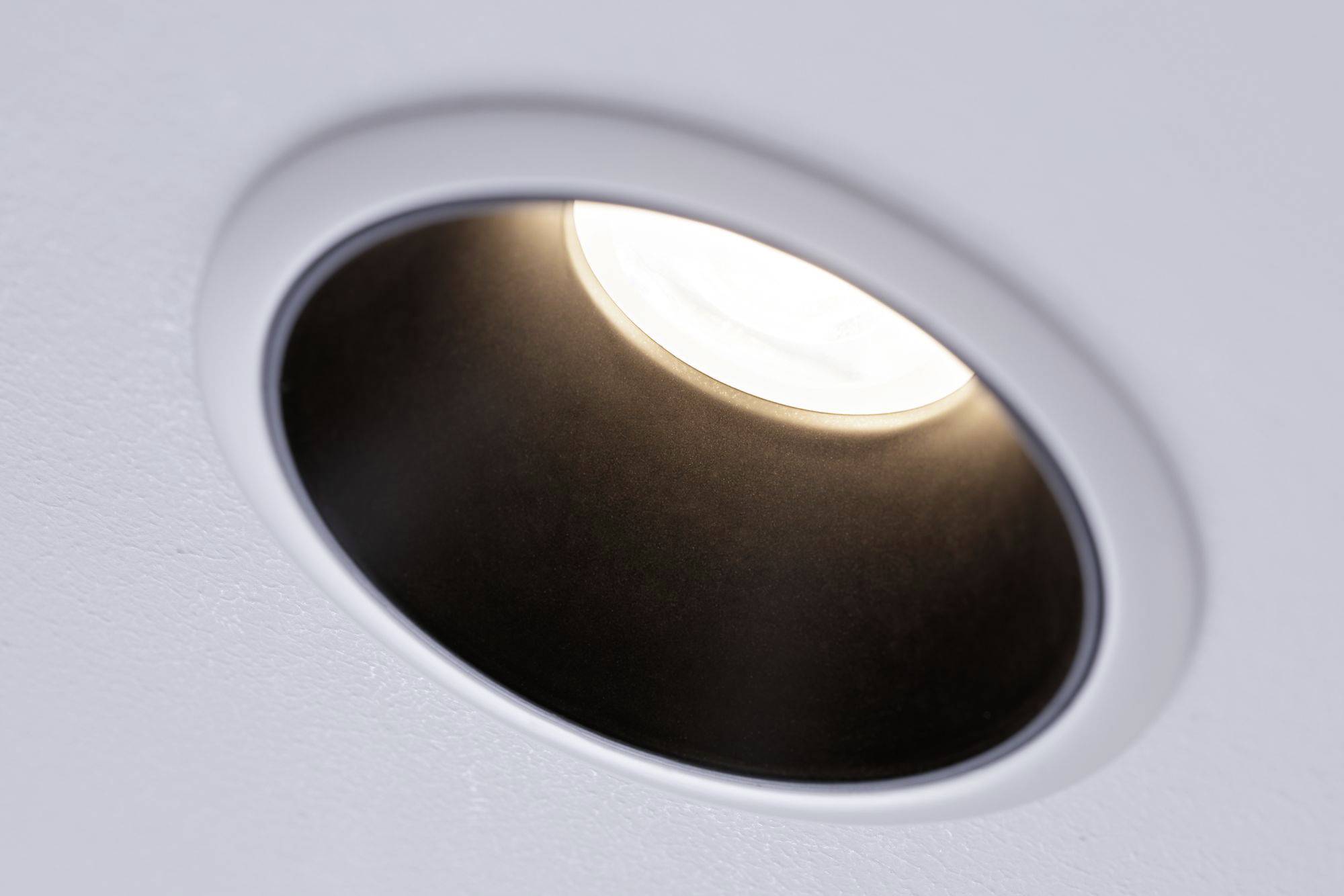 Einbau-Deckenleuchte mit weißem Rahmen, leuchtet warmes Licht in einem modernen Raum, minimalistisch gestaltet.