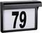 Schwarzes Gehäuse mit weißem Schild, darauf '79' in großen schwarzen Ziffern. Einfache Hausnummernanzeige.