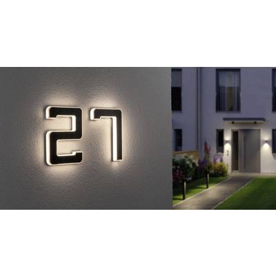 Beleuchtete Hausnummer '27' an einer Hauswand. Im Hintergrund führt ein beleuchteter Weg zu einem modernen Gebäude.