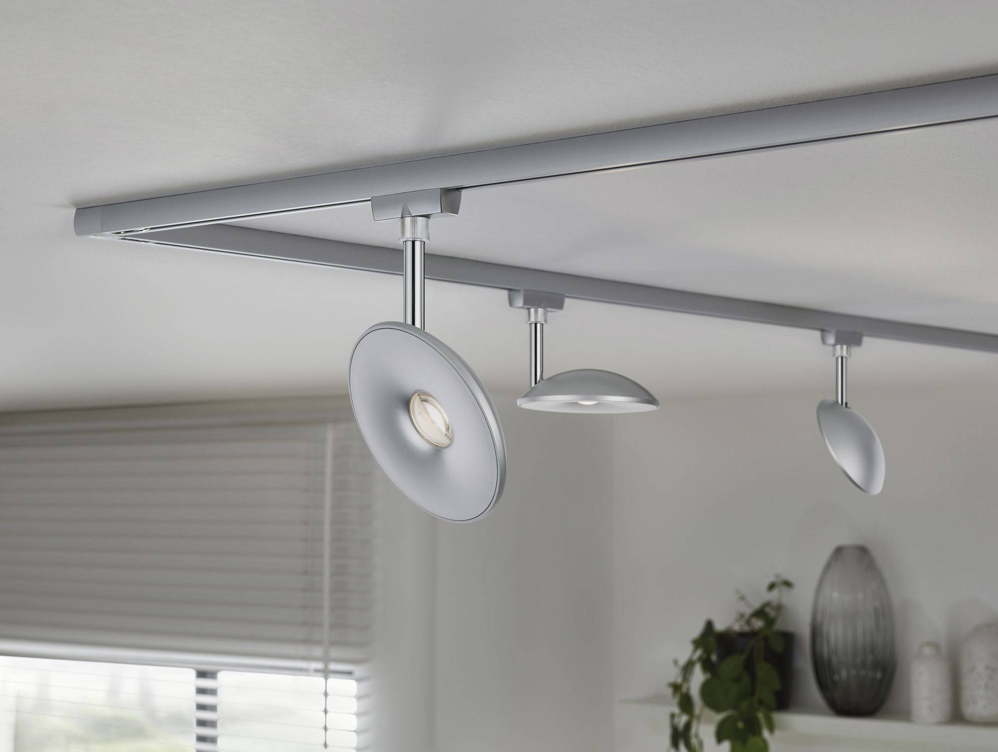 Drei moderne Deckenleuchten in einem Wohnzimmer, mit Fenstern und Pflanzen im Hintergrund.
