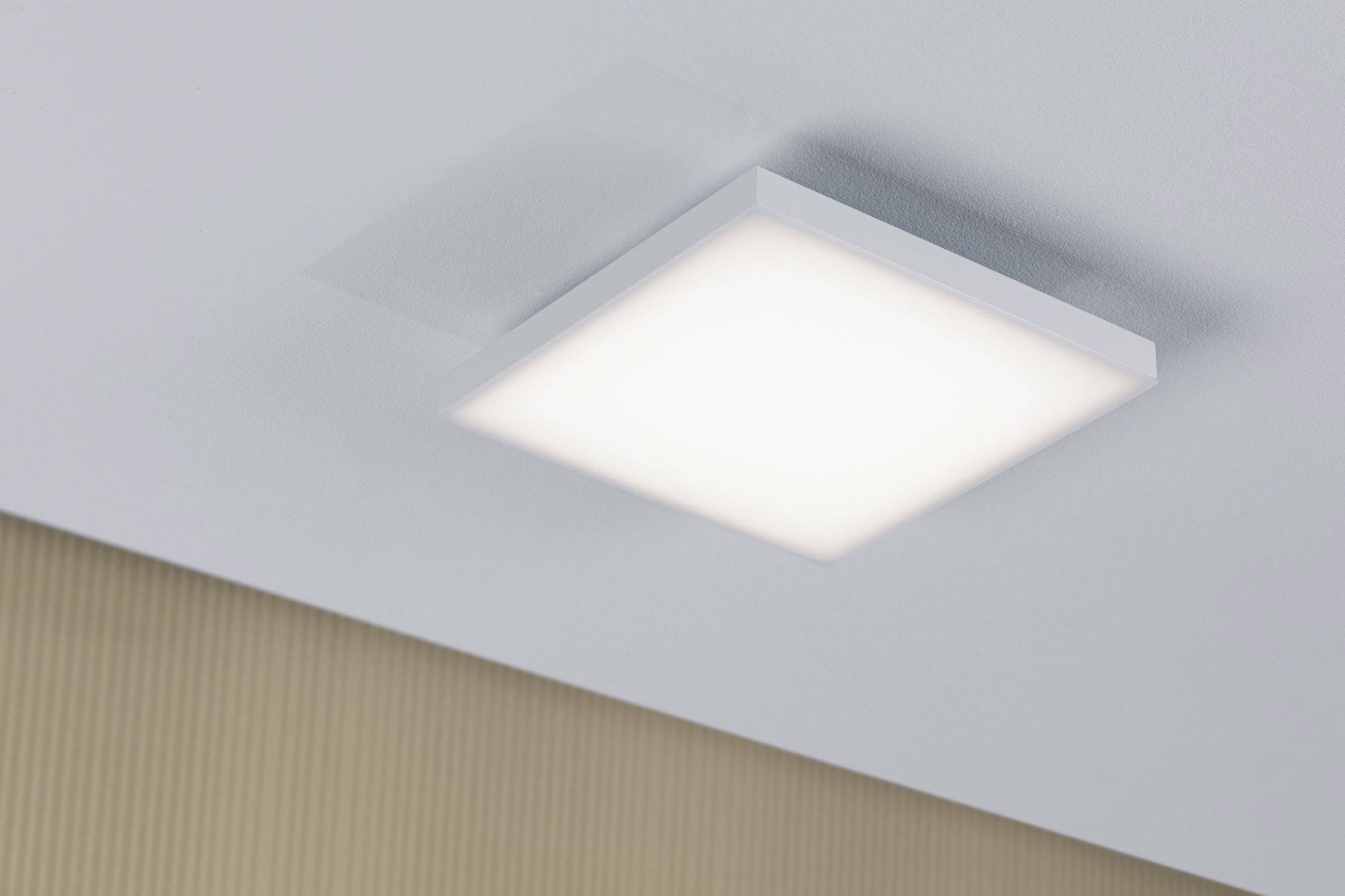 Quadratische Deckenleuchte mit hellem, gleichmäßigem Licht, montiert an einer weißen Decke über einer beigen Wand.