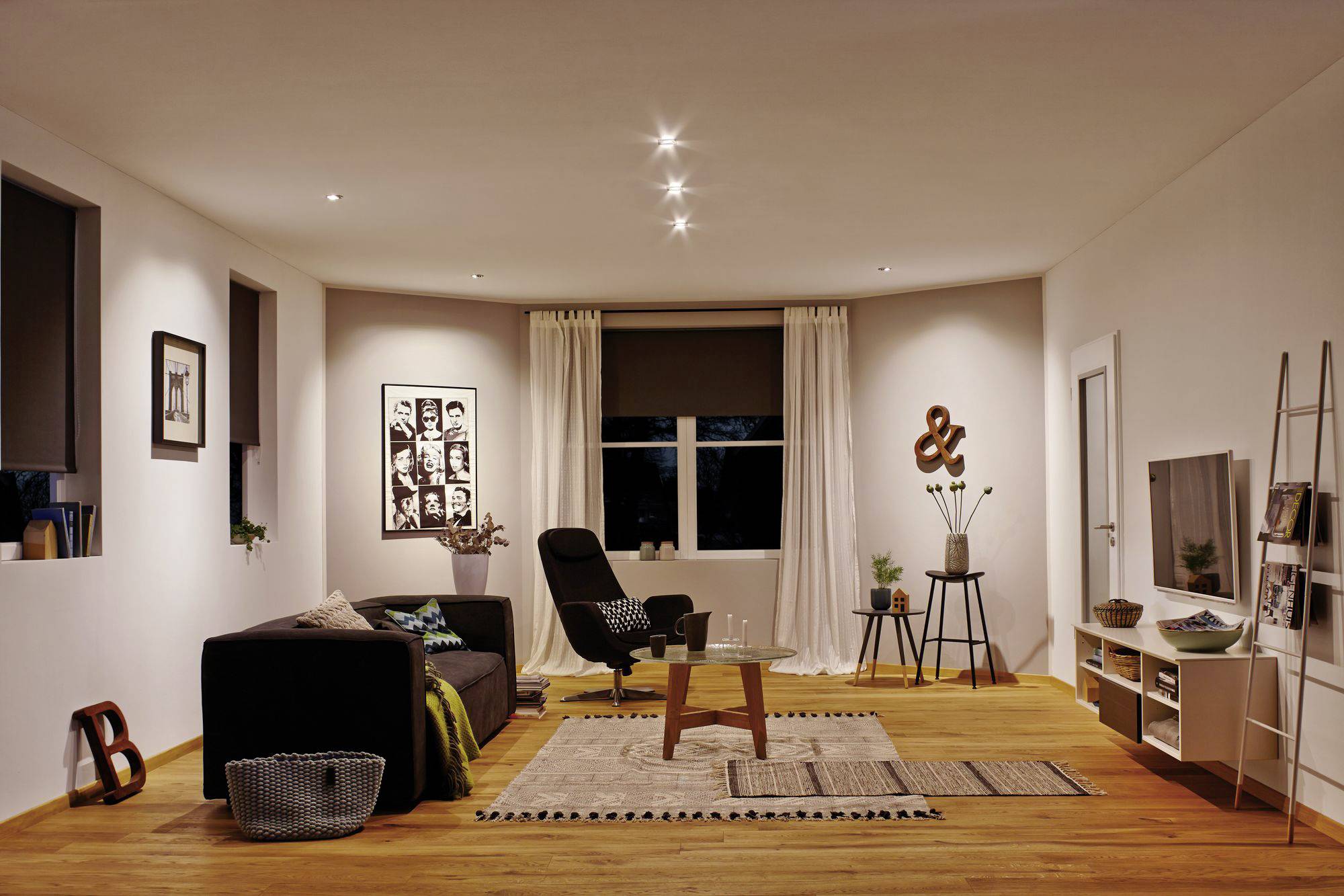 Ein modernes Wohnzimmer mit einem schwarzen Sofa, einem Sessel, mehreren Teppichen und Wanddekorationen. Warme Beleuchtung und Holzboden.
