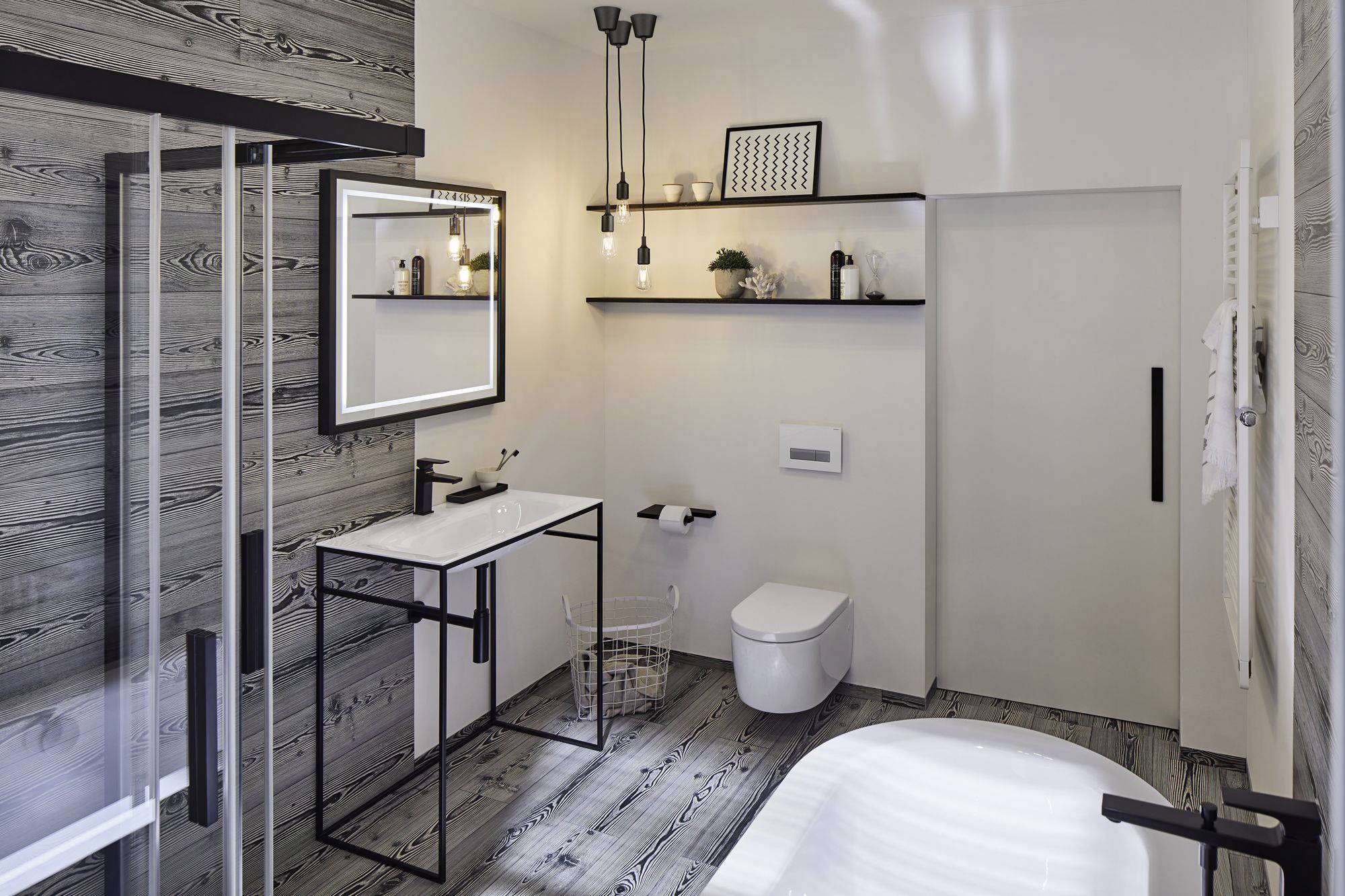 Modernes Badezimmer mit Holzoptikfliesen, freistehender Badewanne, wandhängendem WC und Waschtisch mit beleuchtetem Spiegel.