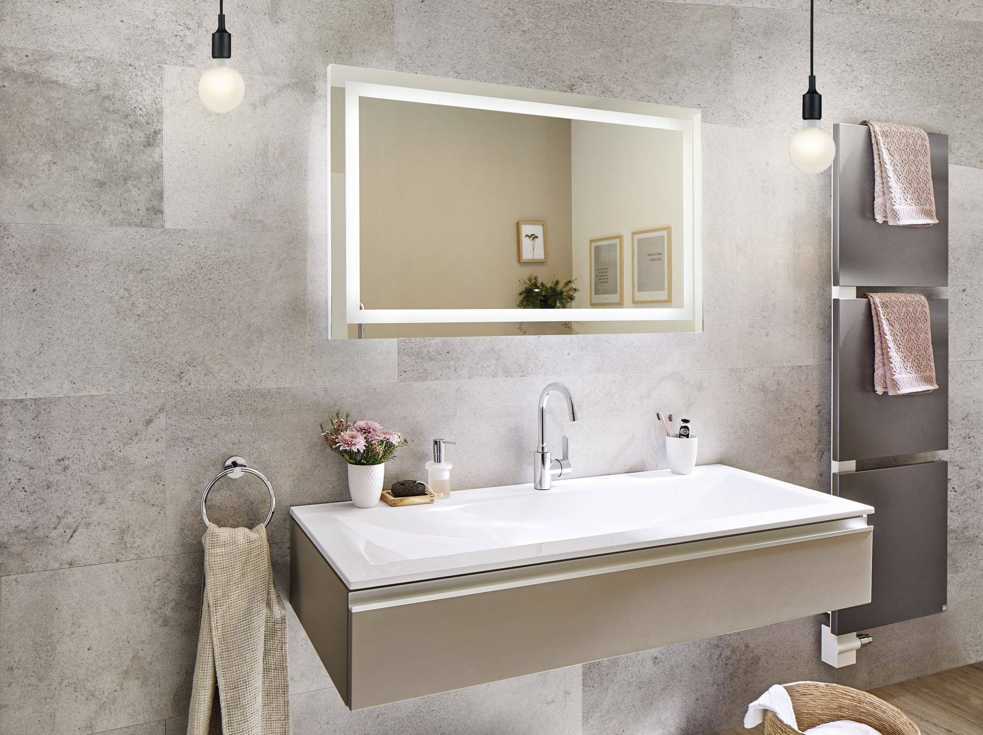 Modernes Badezimmer mit rechteckigem Waschbecken und beleuchtetem Spiegel. An der Wand hängen zwei Handtücher. Dezente Beleuchtung.