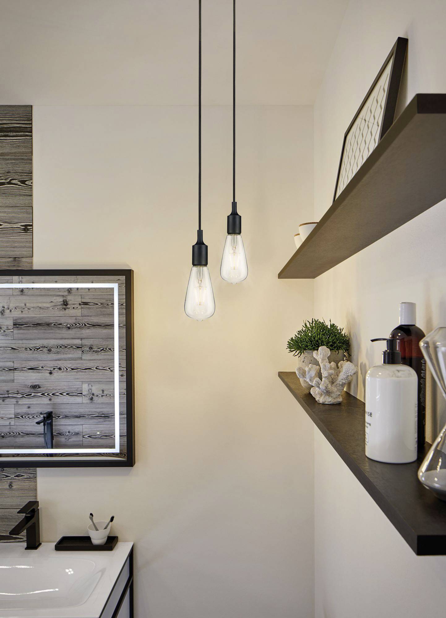 Zwei hängende Glühbirnen beleuchten ein modernes Badezimmer mit einem Spiegel und dekorativen Regalen.