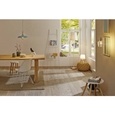 Ein modernes Wohnzimmer mit einem Holztisch, weißen Stuhl, Stehlampe und Bücherregal. Große Fenster lassen Tageslicht herein.