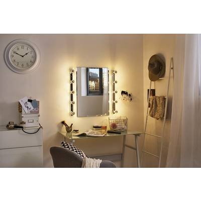 Gemütlicher Schminktisch mit beleuchtetem Spiegel, Uhr an der Wand, Hocker und diversen Beauty-Artikeln in einem warm beleuchteten Raum.