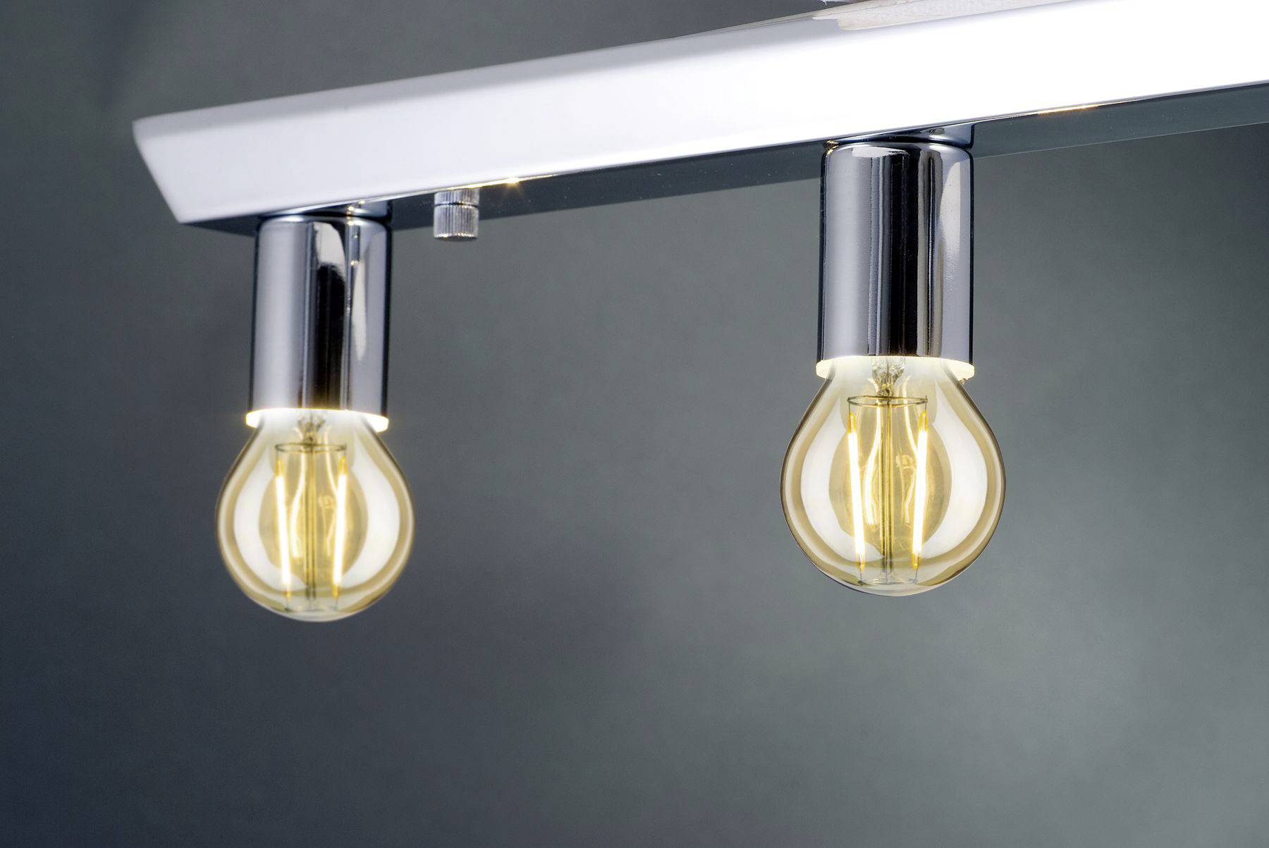 Zwei leuchtende Glühbirnen hängen an einer glänzenden Metallhalterung vor einem neutralen Hintergrund.