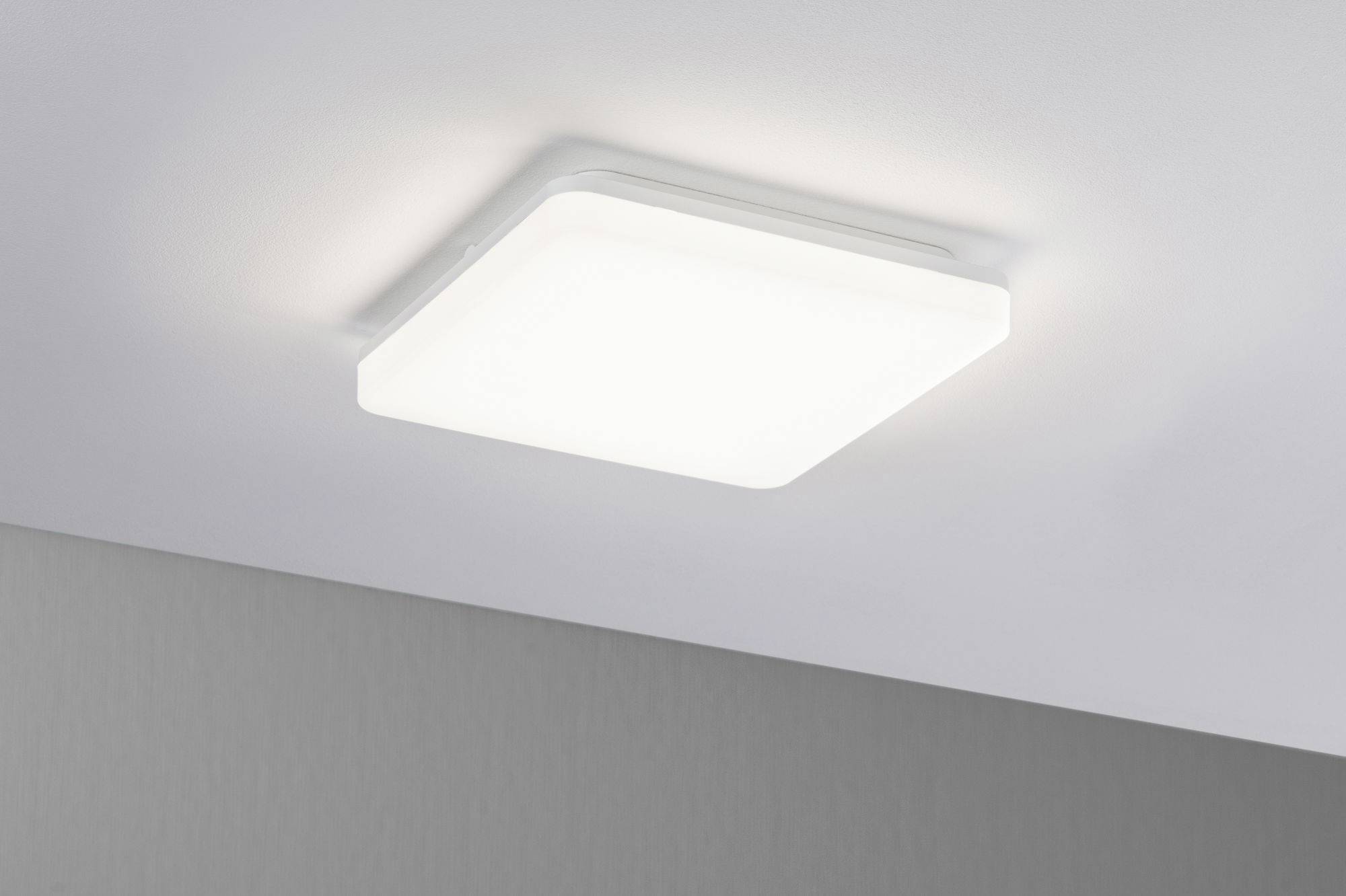 Quadratische, weiße LED-Deckenleuchte an einer grauen Decke, gleichmäßig abstrahlendes Licht. Minimalistisches Design.