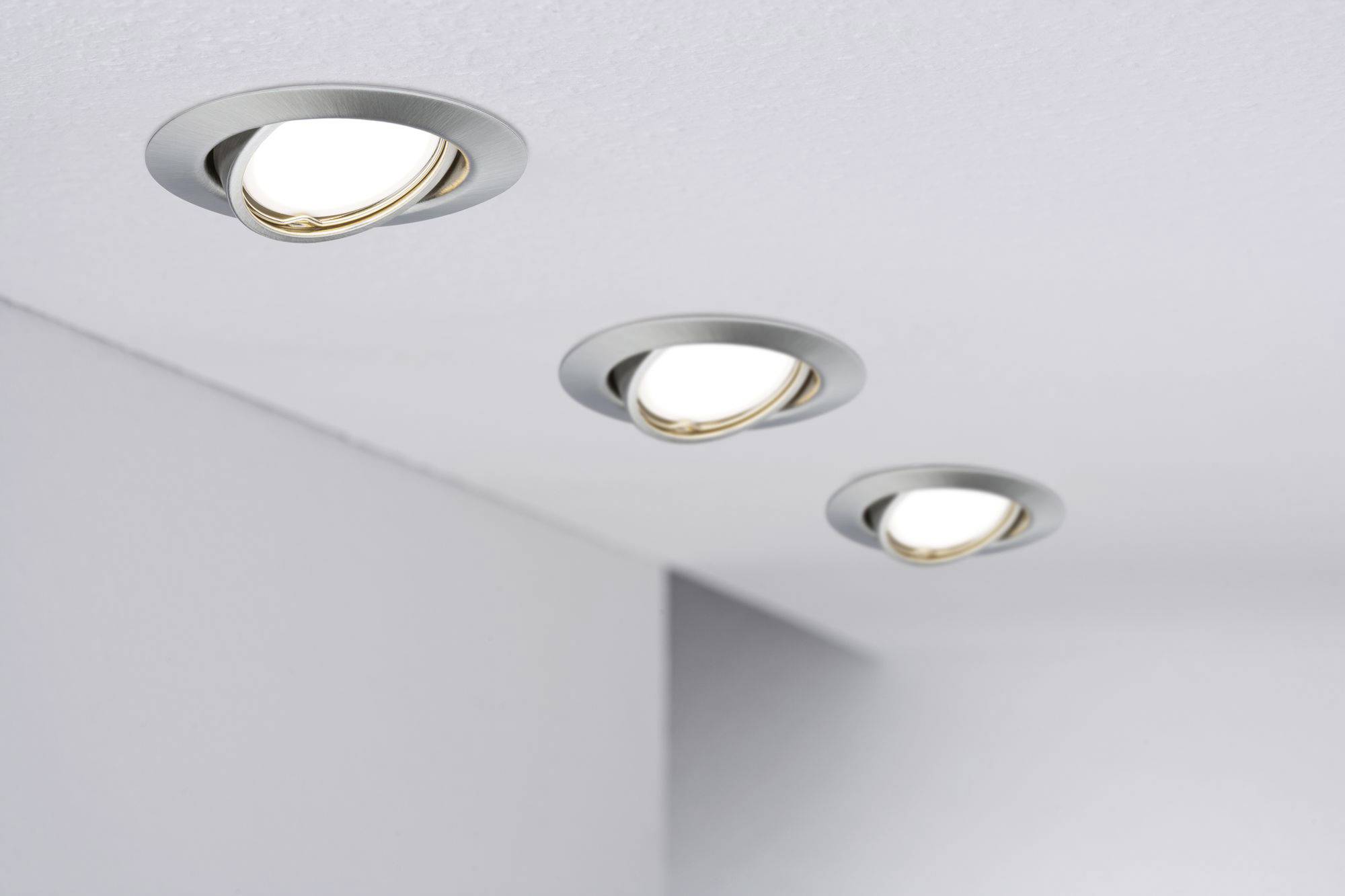 Drei moderne Einbauleuchten mit rundem, metallischem Rahmen sind in einer weißen Decke montiert und strahlen warmes Licht aus.