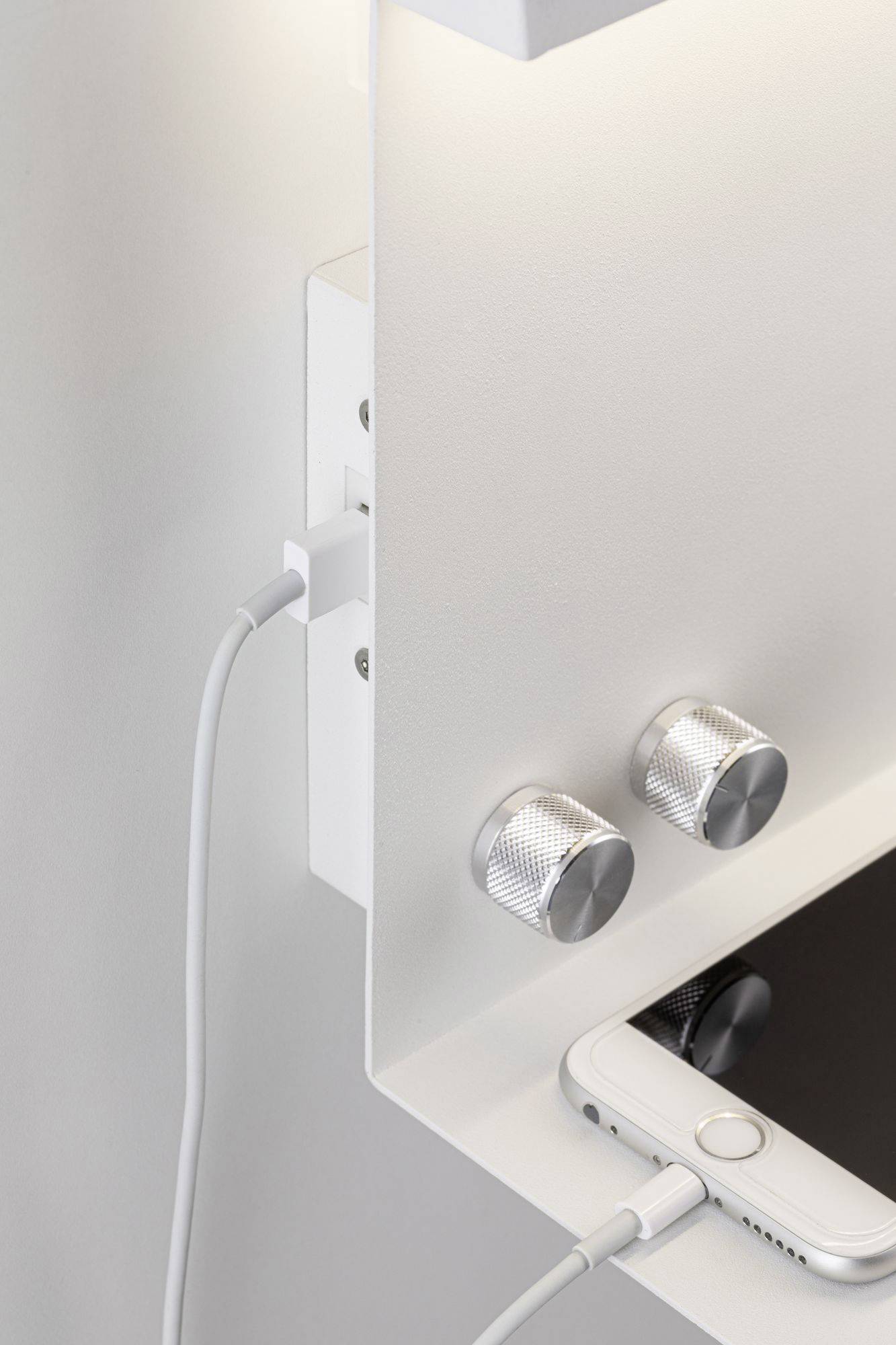 Smartphone auf Regal wird mit Ladegerät verbunden, Regalknöpfe aus Metall.